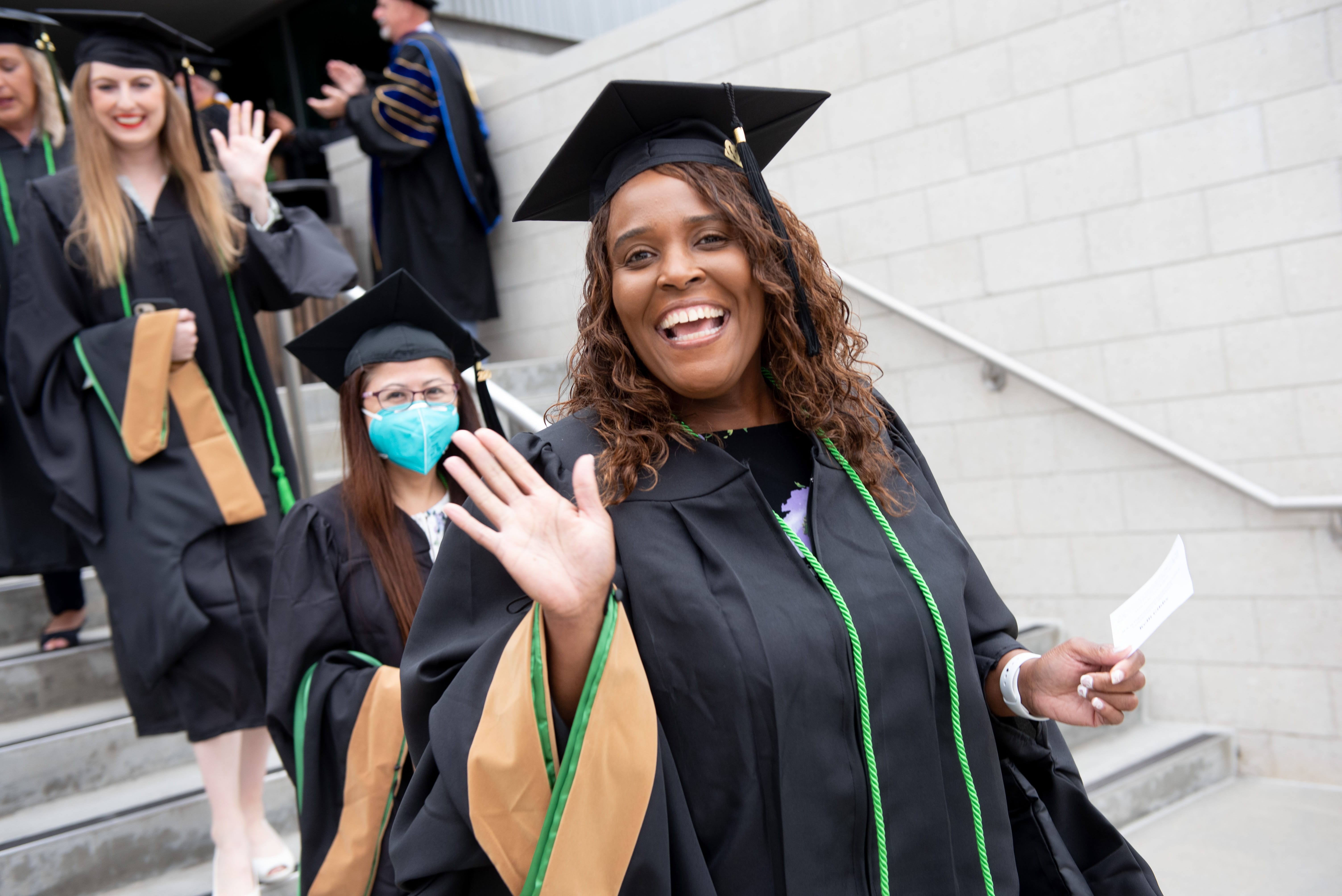 Photo of woman participating in Claremont Lincoln University Commencement wearing a cap and gown and waving.